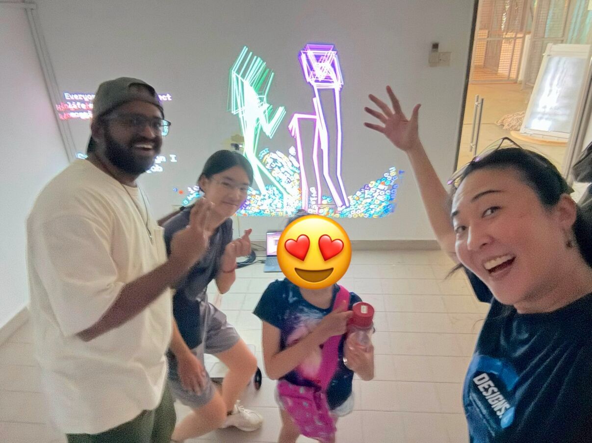 kesh, chrissie choo and two kids in front of the projection, two neon figures and a heap of letters behind them